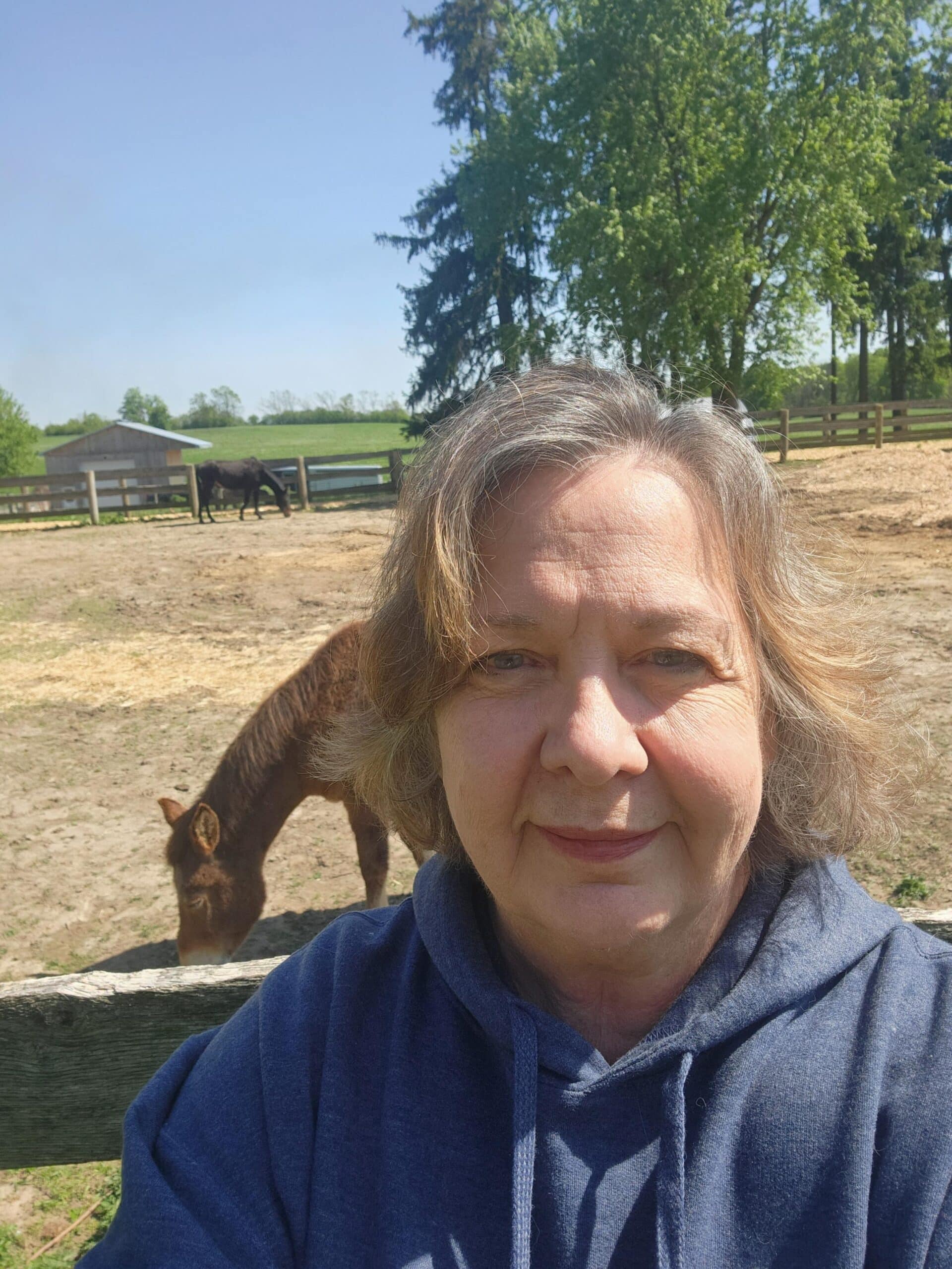 Photo of a woman with a donkey grazing behind her in a field